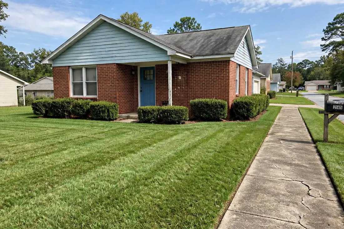 Freshly mowed lawn and neatly trimmed shrubs at the same brick ranch after cleanup